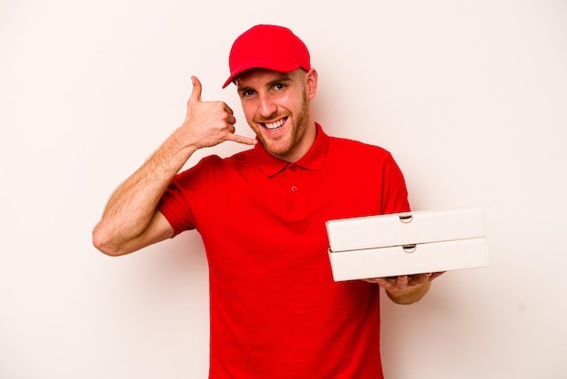 Foto entrega joven hombre caucásico sosteniendo pizzas aislado sobre fondo blanco mostrando un gesto de llamada de teléfono móvil con los dedos