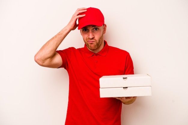 Entrega joven hombre caucásico sosteniendo pizzas aislado sobre fondo blanco sorprendido de haber recordado una reunión importante