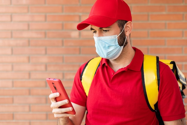 Entrega joven en hombre protector con uniforme rojo usando un teléfono inteligente en la entrada del cliente de la casa Servicio de entrega comercio electrónico y concepto de compras en línea