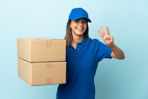 Entrega joven mujer aislada en azul feliz y contando tres con los dedos