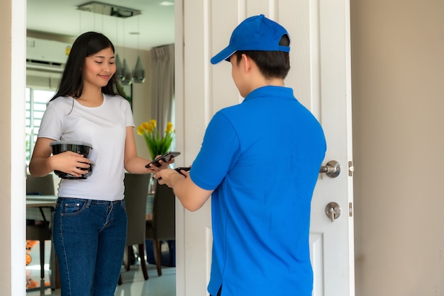 Entrega joven en uniforme azul sonrisa y sosteniendo cajas de comida en el frente de la casa