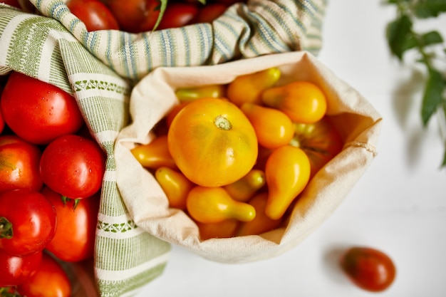 Entrega de mercado de diferentes tipos de tomates en bolsa textil ecológica, Cero desperdicio, Fondo ecológico, Surtido de tomates, mercado de agricultores locales, Hortalizas frescas, cosecha. Vista superior, espacio de copia.