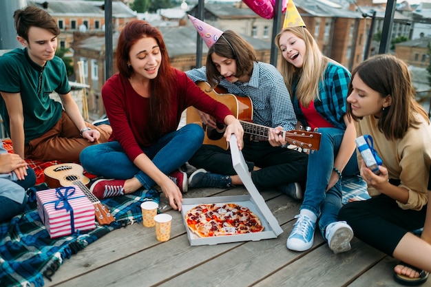 Foto entrega de pizza a la azotea. comida de cumpleaños poco convencional. preferencias alimentarias de los jóvenes. comida sabrosa y deliciosa. adolescentes hambrientos felices