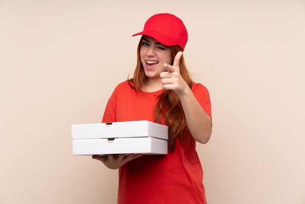 Entrega de pizza chica adolescente sosteniendo una pizza señala con el dedo