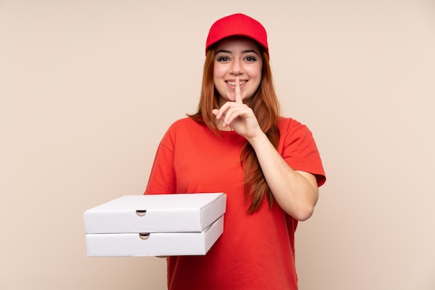 Entrega de pizza chica adolescente sosteniendo una pizza sobre pared aislada haciendo gesto de silencio