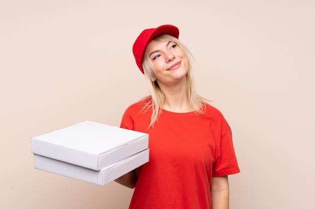 Entrega de pizza Mujer rusa sosteniendo una pizza sobre una pared aislada mirando hacia arriba mientras sonríe