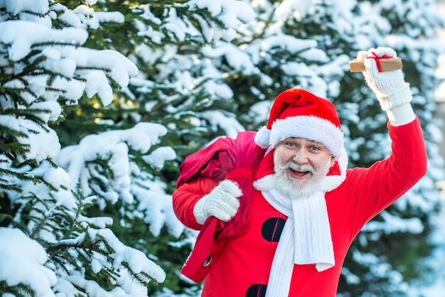 Entrega presentes de Natal Papai Noel vindo para a floresta de inverno com um saco de presentes na neve landsca ...