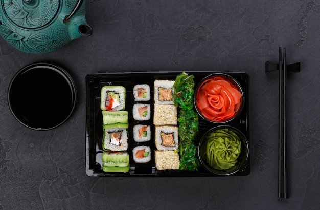 Entrega de restaurante japonés, vista superior de la caja para llevar, maki de sushi y juego de rollos. Palillos, jengibre, salsa de soja, wasabi. Comidas en fondo negro