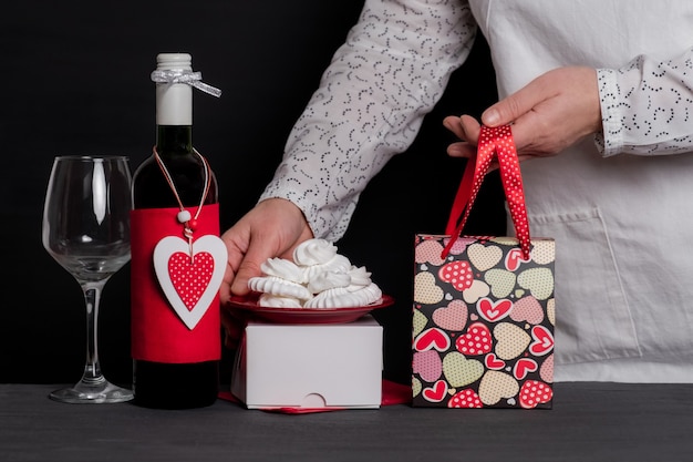 Entrega sosteniendo una bolsa festiva cerca de una botella de vino con un corazón rojo del día de San Valentín y pasteles