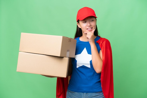 Entrega de superhéroe Mujer asiática sosteniendo cajas sobre un fondo aislado mirando hacia un lado y sonriendo