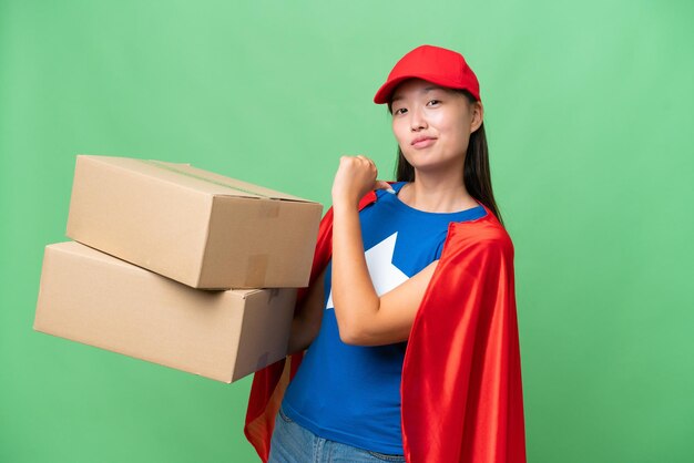 Entrega de superhéroe Mujer asiática sosteniendo cajas sobre un fondo aislado orgullosa y satisfecha de sí misma