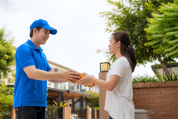 Entregador asiático jovem de uniforme azul dando uma caixa para o cliente