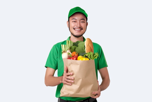 Entregador asiático vestindo uniforme verde, segurando o saco de papel de alimentos frescos isolado no espaço em branco.