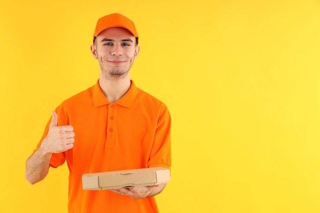 Entregador atraente com caixa de pizza em fundo amarelo