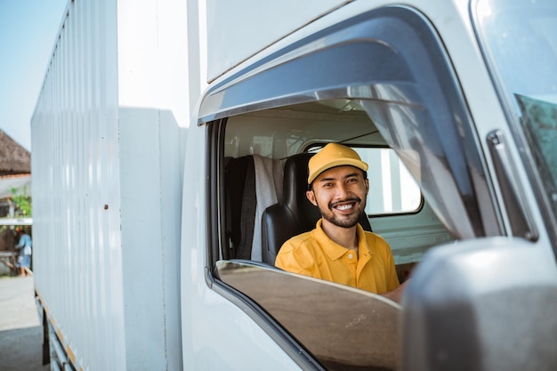 Foto entregador barbudo em uniforme amarelo sorrindo enquanto dirige caminhão de mercadorias