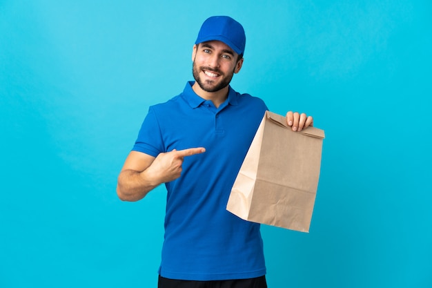 Entregador com barba isolada na parede azul e apontando-o