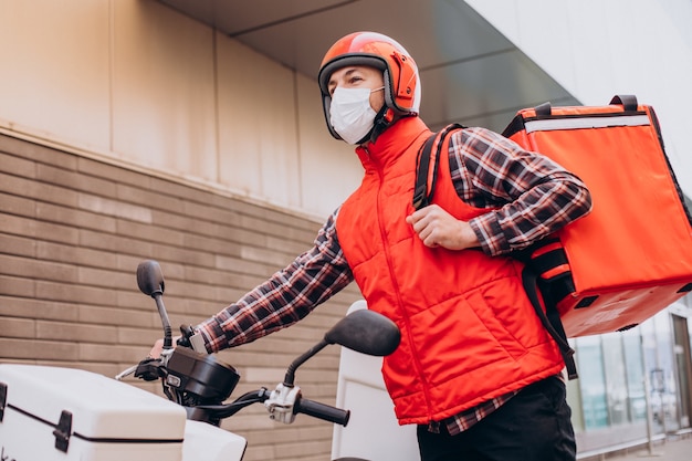 Entregador de comida dirigindo scooter com caixa com comida e usando máscara