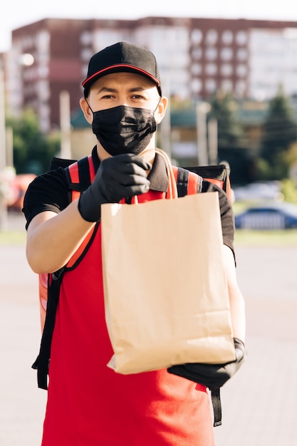 Foto entregador de comida segurando um saco de papel com comida na rua entregador em casa ao ar livre com máscara protetora