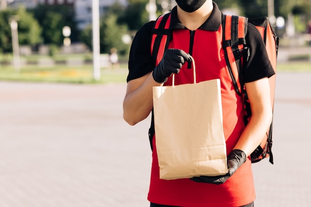Entregador de comida segurando um saco de papel com comida na rua. Entregador em casa ao ar livre em proteção