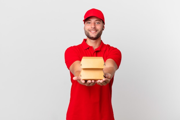 Entregador de hambúrguer sorrindo feliz com simpatia e oferecendo e mostrando um conceito