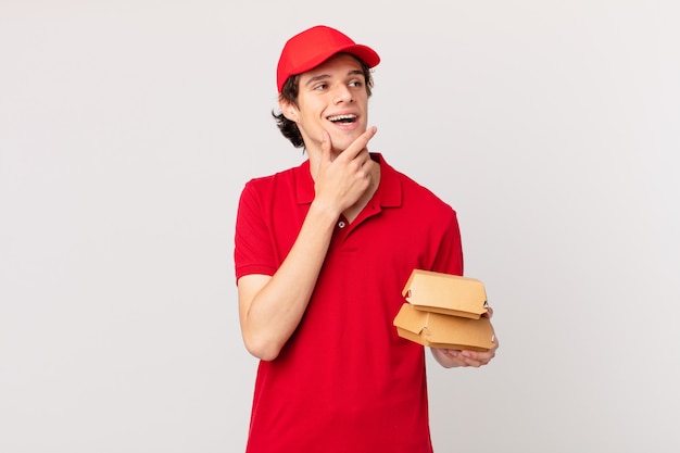 Entregador de hambúrguer sorrindo feliz e sonhando acordado ou duvidando