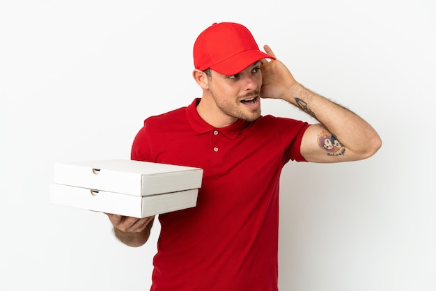 Entregador de pizza com uniforme de trabalho pegando caixas de pizza em uma parede branca isolada e ouvindo algo colocando a mão na orelha