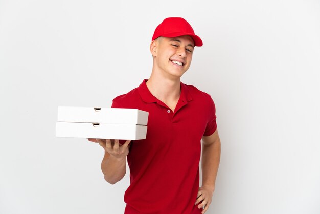 Entregador de pizza com uniforme de trabalho pegando caixas de pizza isoladas no fundo branco, posando com os braços na cintura e sorrindo