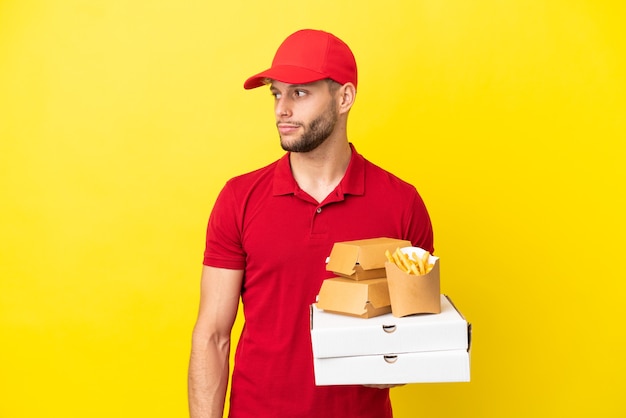Entregador de pizza pegando caixas de pizza e hambúrgueres sobre um fundo isolado olhando para o lado