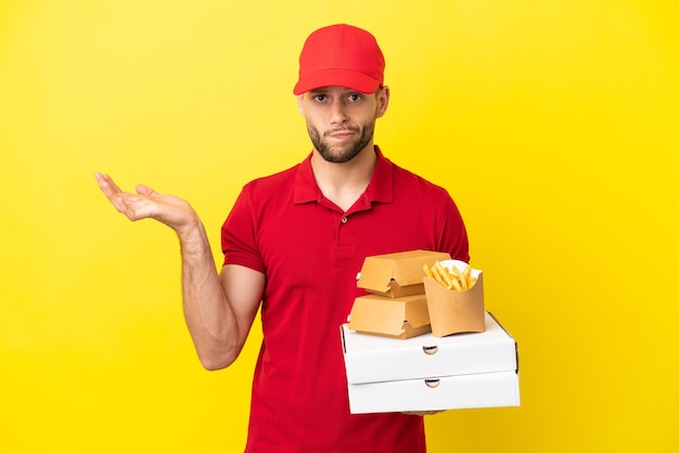 Entregador de pizza pegando caixas de pizza e hambúrgueres sobre um fundo isolado, tendo dúvidas enquanto levanta as mãos