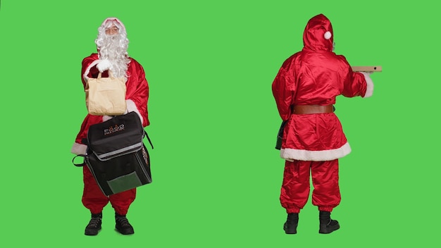 Entregador de terno vermelho de papai noel carregando mochila com caixa de pizza e pedido de saco de papel, conceito de entrega de véspera de natal. Personagem de nick de santo jovem contra pano de fundo de tela verde de corpo inteiro.