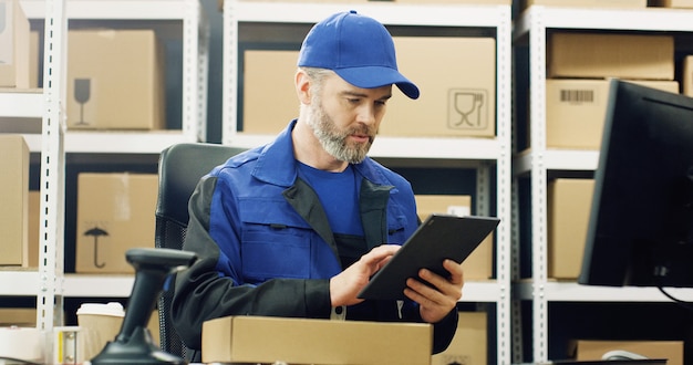 entregador de uniforme e boné trabalhando no dispositivo de tablet nos correios.