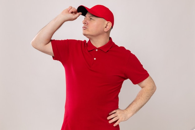 Foto entregador de uniforme vermelho e boné olhando para o lado com uma cara séria