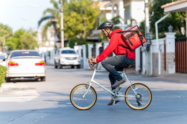 Entregador de uniforme vermelho Pedalando para entregar produtos aos clientes em casa.