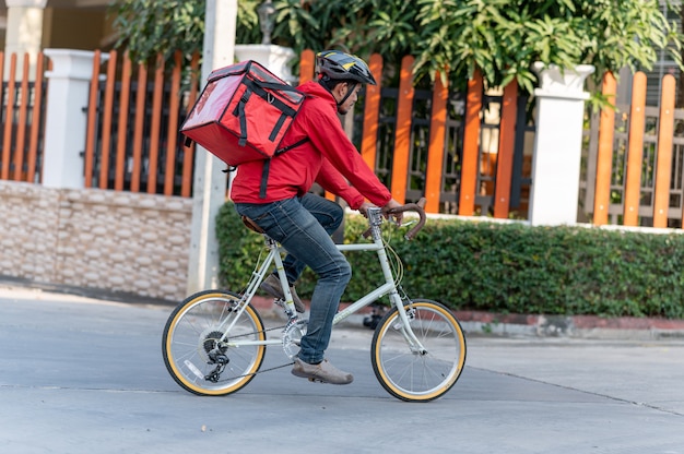 Entregador de uniforme vermelho Pedalando para entregar produtos aos clientes em casa.