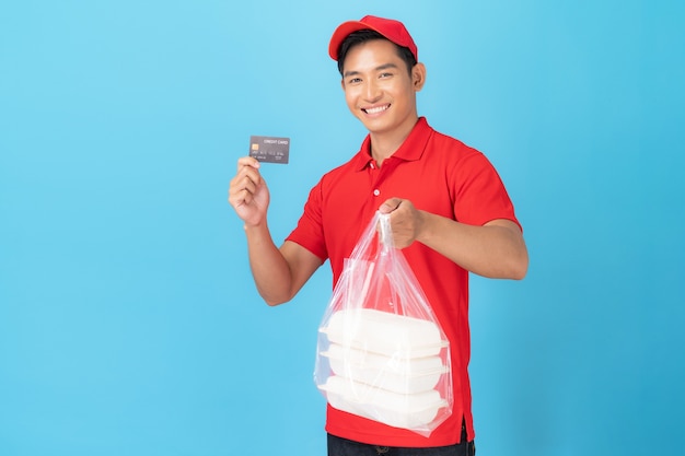 Entregador em uniforme de camisa pólo vermelha em pé com pedido de comida com cartão de crédito