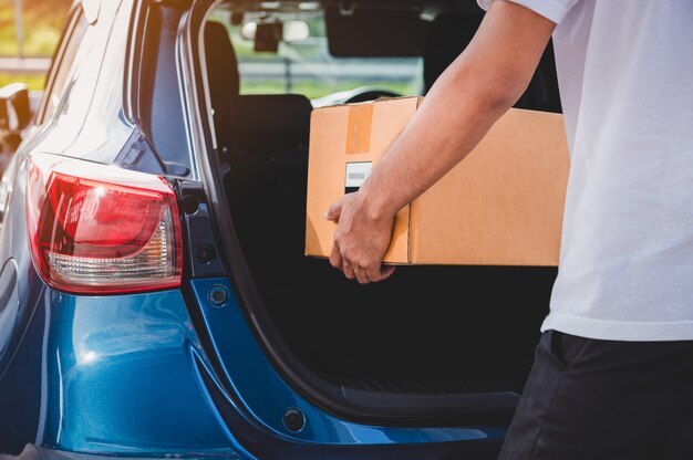 Entregador está entregando caixa de papelão para os clientes através da porta do porta-malas do carro