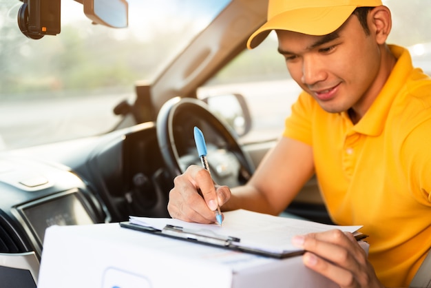 Entregador feliz em camisa polo amarela uniforme com caixa de papelão de parcelas no carro