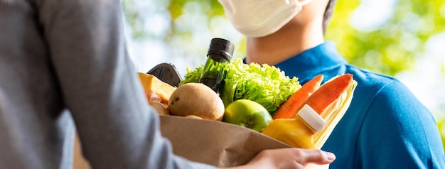 Entregador higiênico usando máscara facial entregando mantimentos ao cliente em casa, entrega de comida no tempo do conceito de pandemia