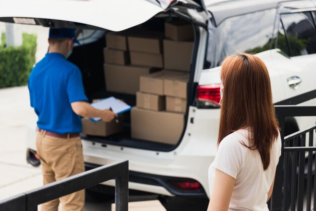 Foto entregador jovem asiático, correio, compras on-line, entrega caixa postal de encomendas, máscara facial protetora e cliente de serviço, mulher, recebendo encaixotado na porta da frente de casa, sob toque de recolher, pandemia de coronavírus covid-19