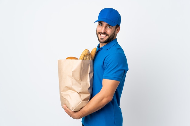 Entregador, segurando um saco cheio de pães isolados na parede branca, sorrindo muito