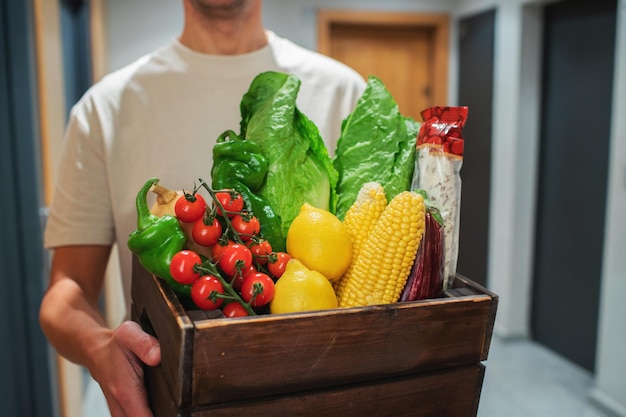 Foto entregador segurando um saco de papel com comida na entrada. o mensageiro entrega a caixa com vegetais e frutas frescas ao cliente