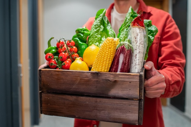 Entregador segurando um saco de papel com comida na entrada. O mensageiro entrega a caixa com vegetais e frutas frescas ao cliente