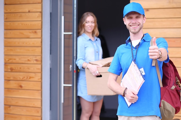 Entregador sorridente em uniforme azul entregando caixa de encomendas ao conceito de serviço de correio destinatário