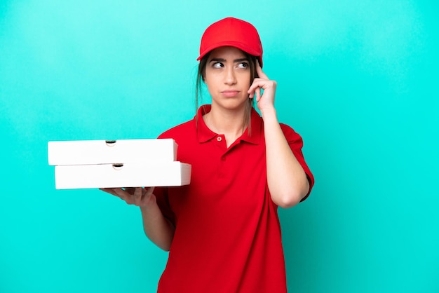 Entregadora de pizza com uniforme de trabalho pegando caixas de pizza isoladas em fundo azul com dúvidas e pensando