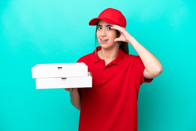 Entregadora de pizza com uniforme de trabalho pegando caixas de pizza isoladas em fundo azul fazendo gesto de surpresa enquanto olha para o lado