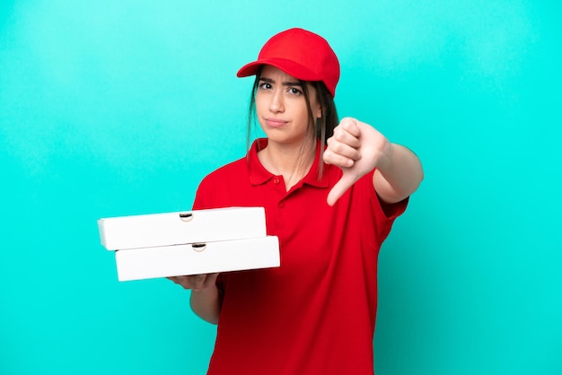 Entregadora de pizza com uniforme de trabalho pegando caixas de pizza isoladas em fundo azul mostrando o polegar para baixo com expressão negativa