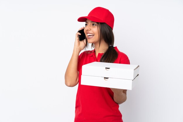 Entregadora de pizza jovem sobre branco, mantendo uma conversa com o telefone móvel