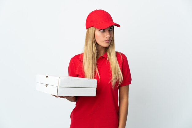 Entregadora de pizza segurando uma pizza isolada na parede branca olhando para o lado