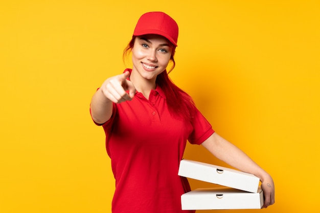 Entregadora de pizza, segurando uma pizza sobre fundo isolado, apontando a frente com expressão feliz