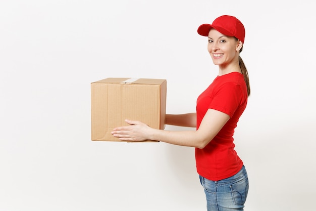 Entregadora de uniforme vermelho, isolado no fundo branco. Mulher de boné, camiseta, jeans trabalhando como mensageiro ou revendedor segurando uma caixa de papelão. Recebendo pacote. Copie o espaço para anúncio. Vista lateral